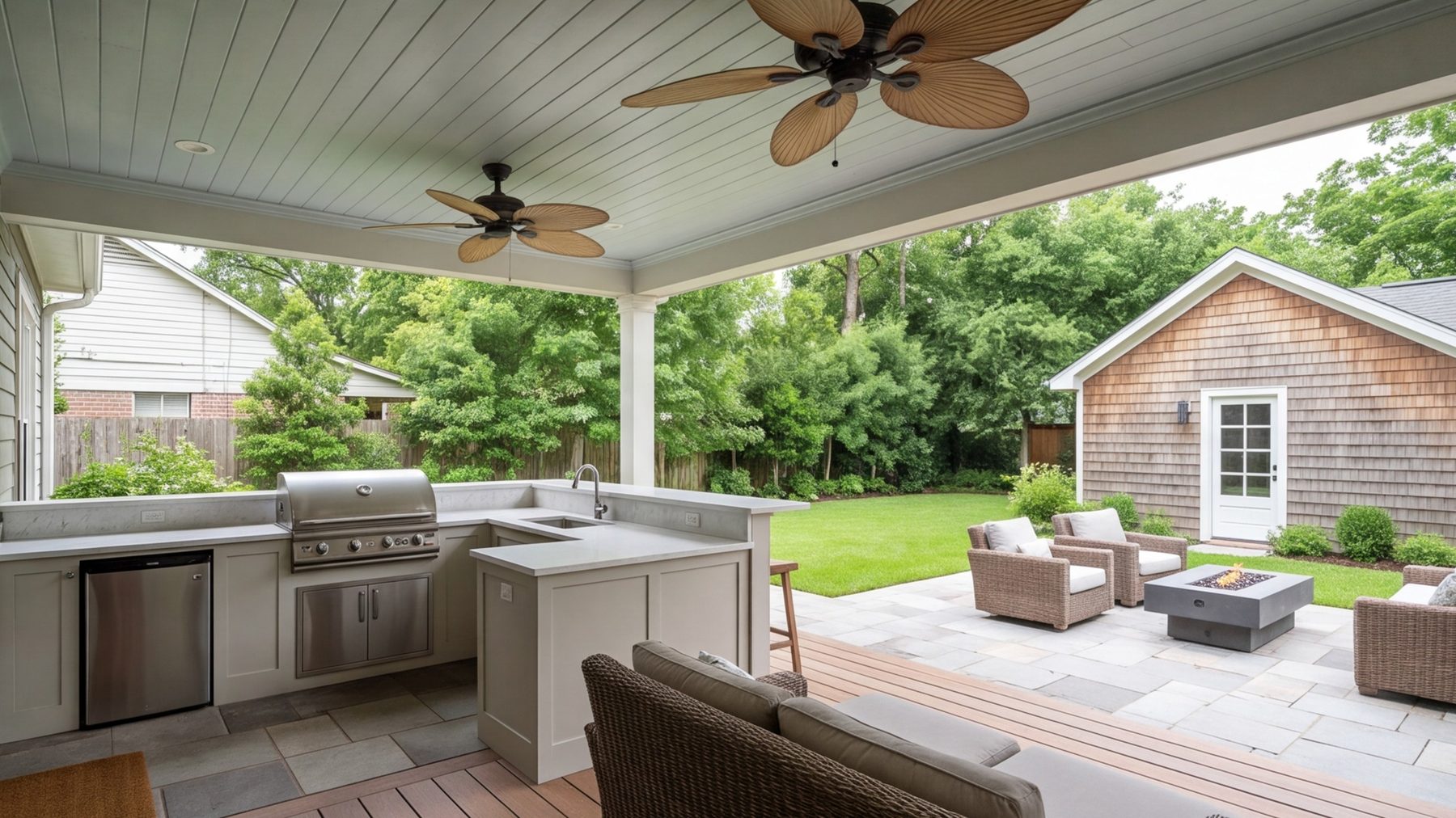 wide covered patio with an outdoor kitchen, seating and fans, lawn and the back of a cottage beyond